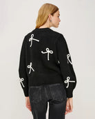 a woman wearing a black button down cardigan with white bow patterns 