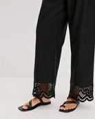 a woman wears black cotton pants with embroidered lacey trim on the hem