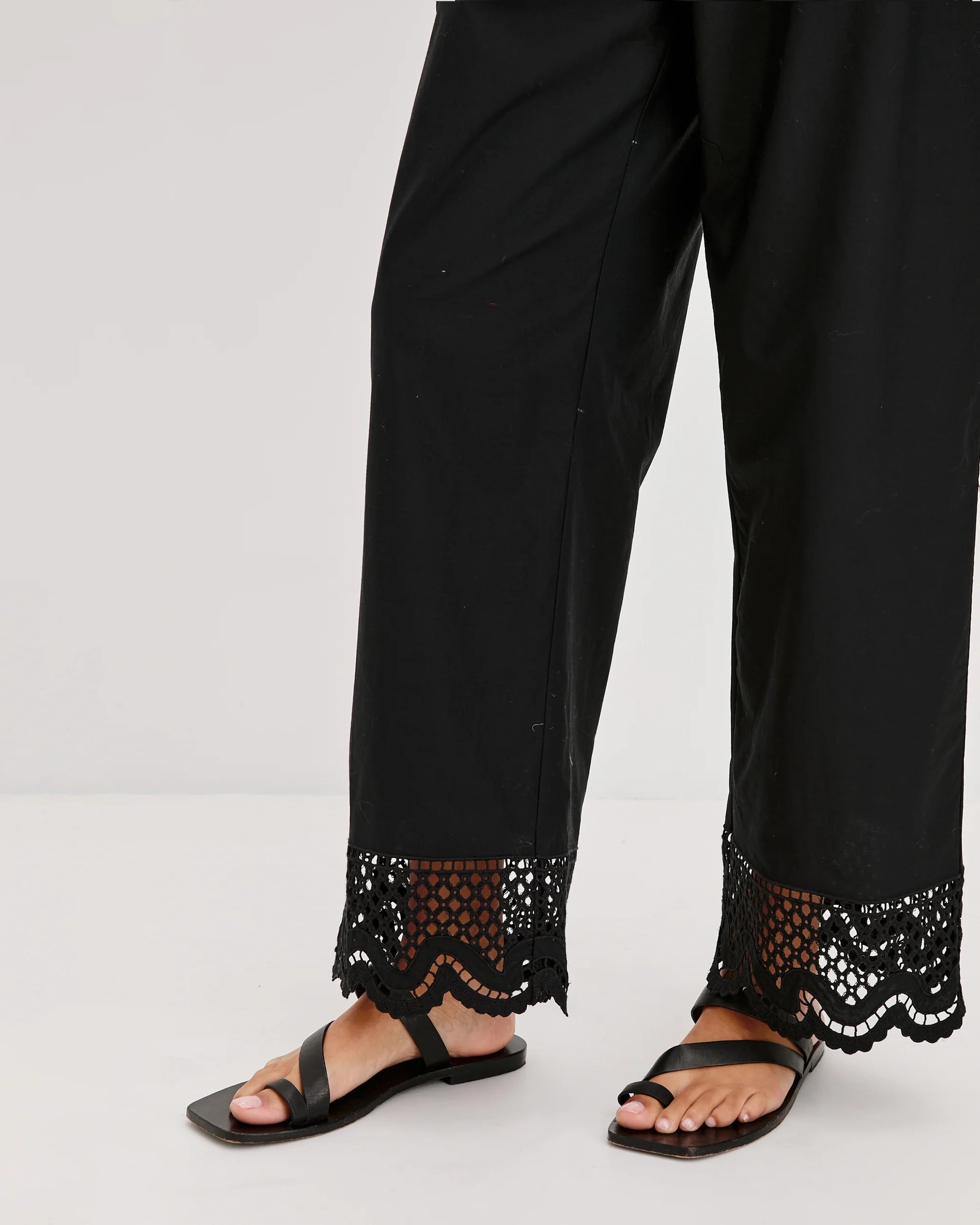 a woman wears black cotton pants with embroidered lacey trim on the hem