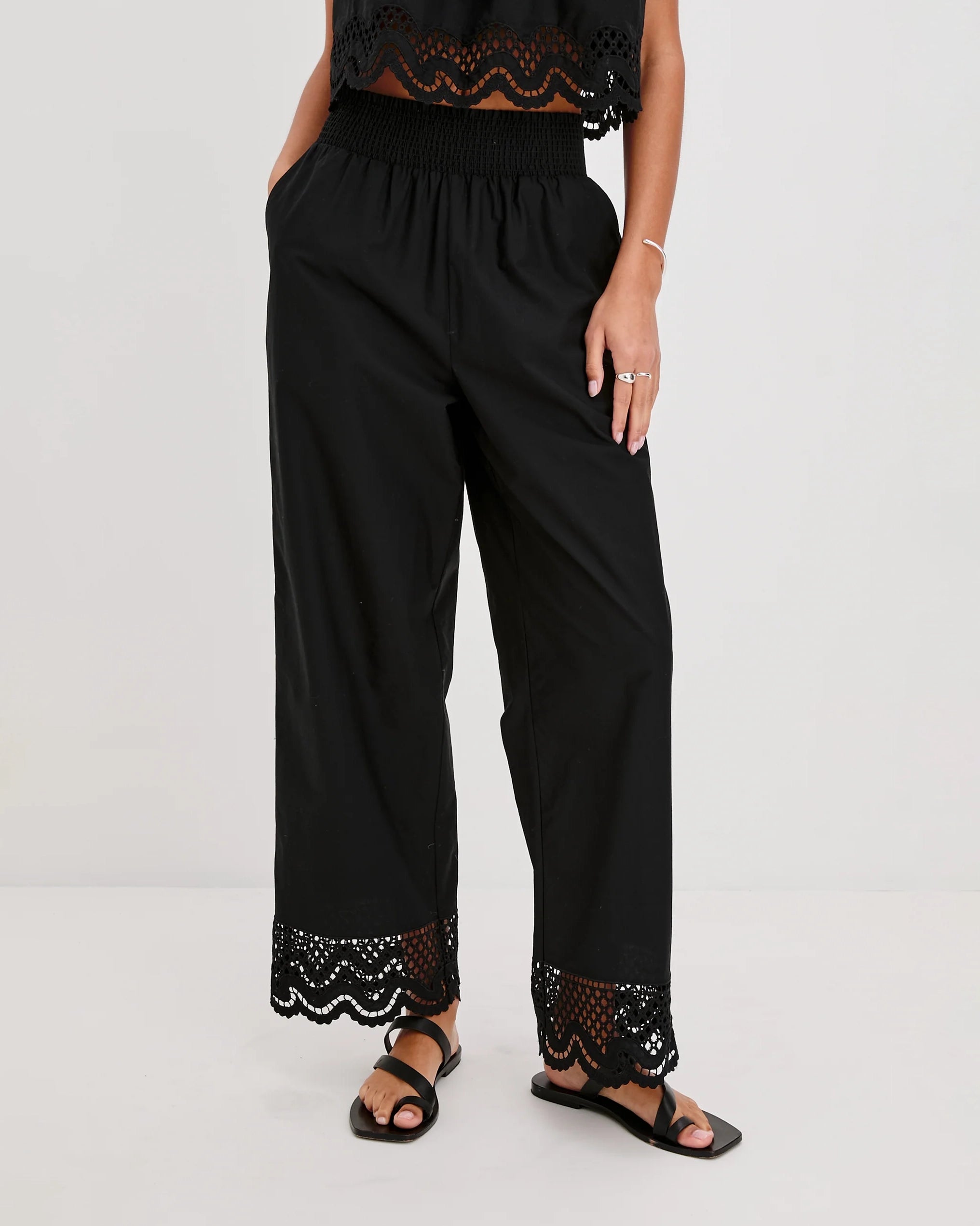 a woman wears black cotton pants with embroidered lacey trim on the hem