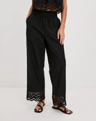 a woman wears black cotton pants with embroidered lacey trim on the hem