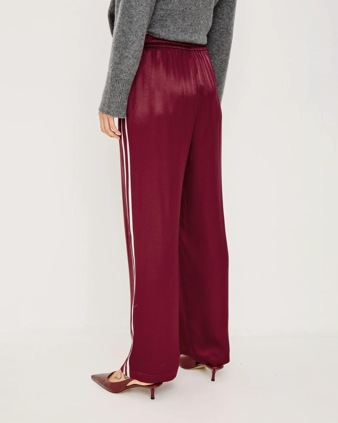 A woman wears maroon satin pants with white stripes