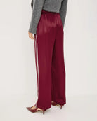A woman wears maroon satin pants with white stripes