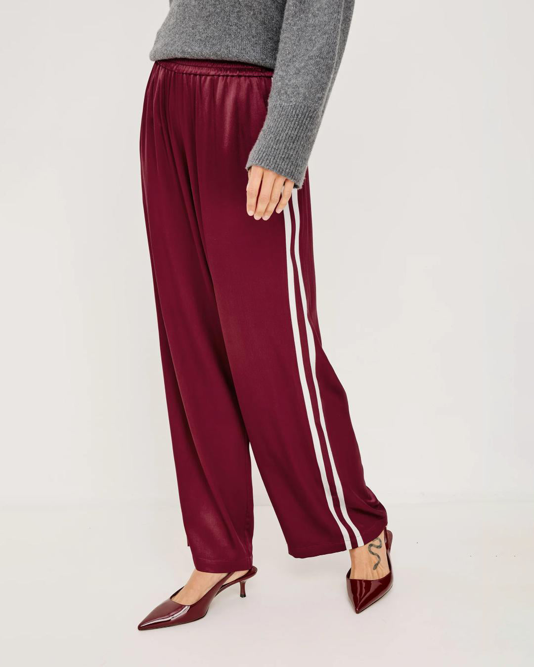 A woman wears maroon satin pants with white stripes