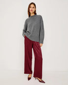 A woman wears maroon satin pants with white stripes with grey sweater