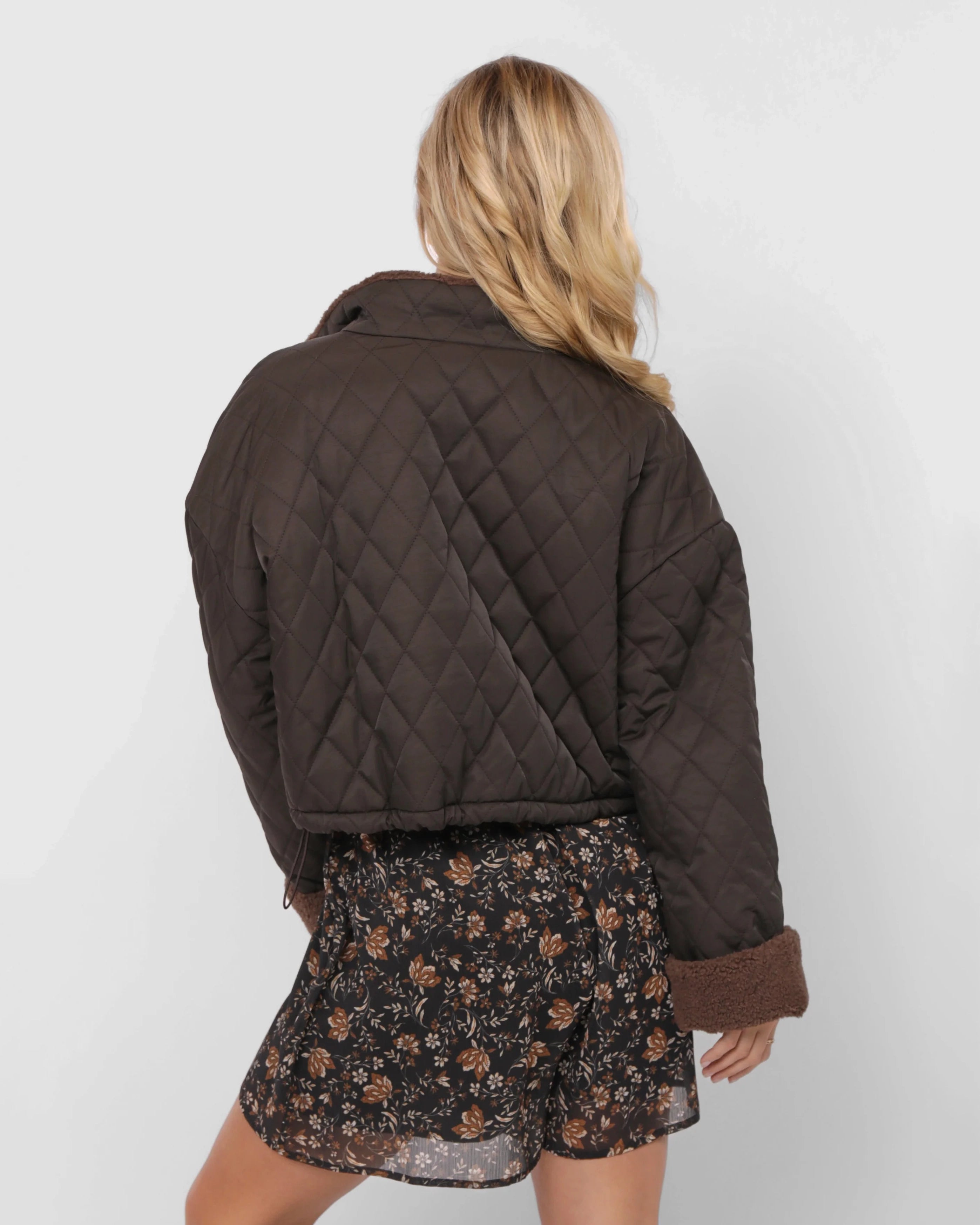 Woman wearing a brown quilted jacket over a floral dress 