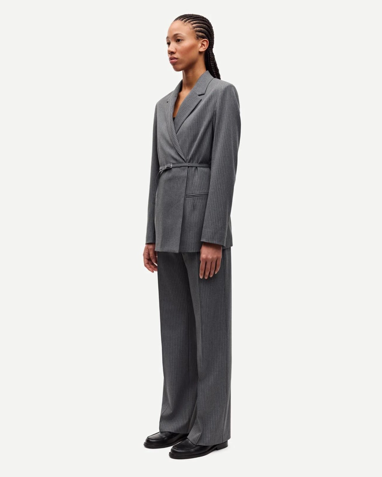 Woman wearing a gray pinstripe suit blazer and matching trousers with belt