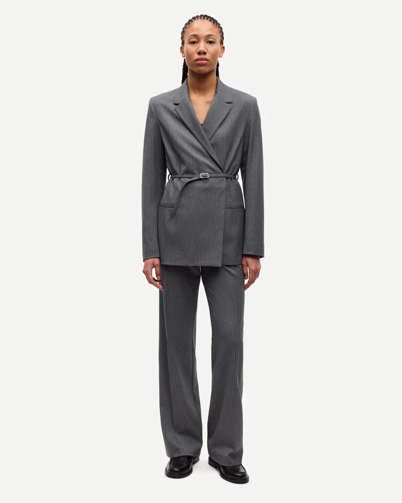 Woman wearing a gray pinstripe suit blazer and matching trousers with belt