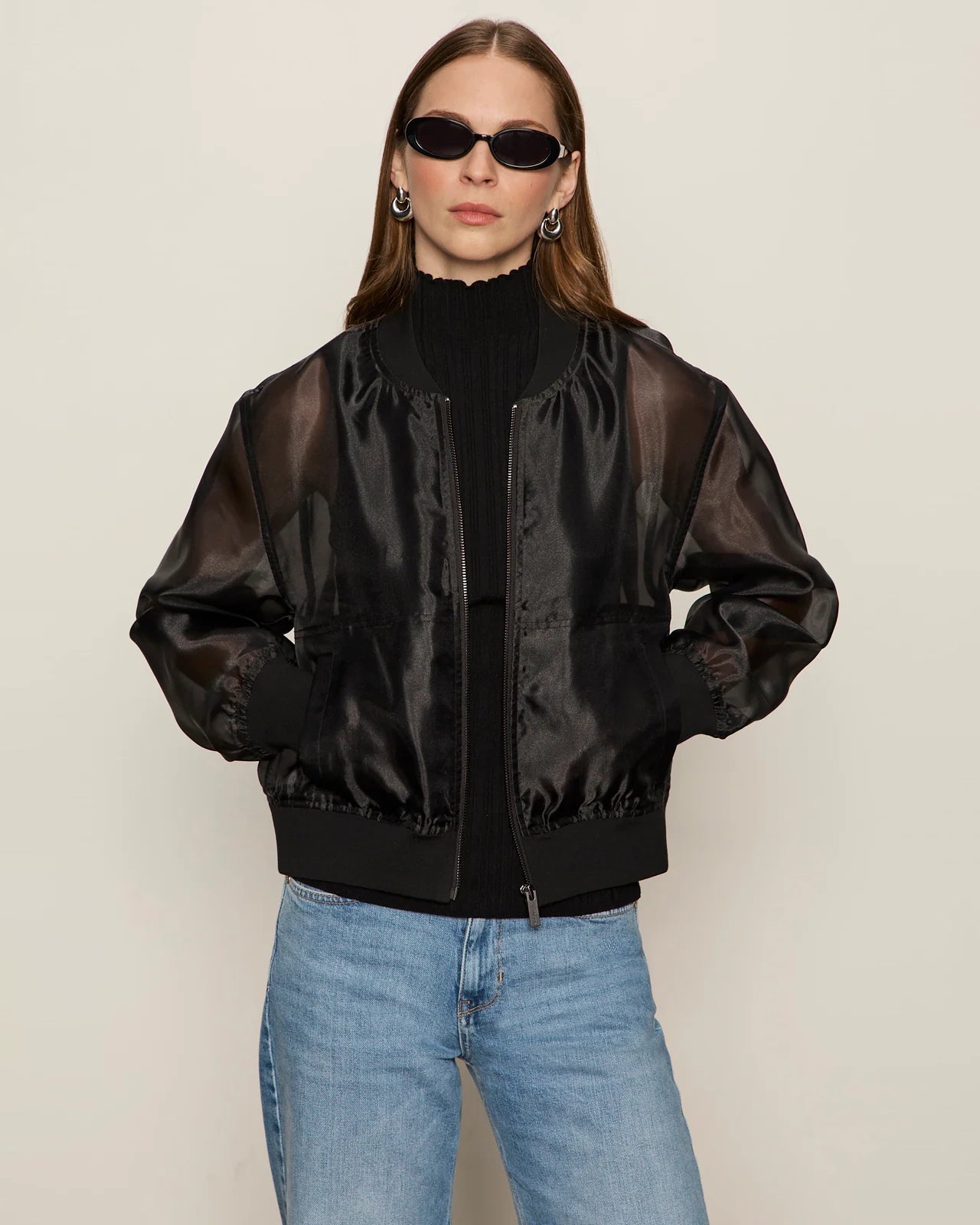 woman wearing a black sheer organza jacket over a black turtleneck and blue jeans