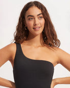Woman wearing a black one-piece swimsuit with one shoulder design by Seafolly