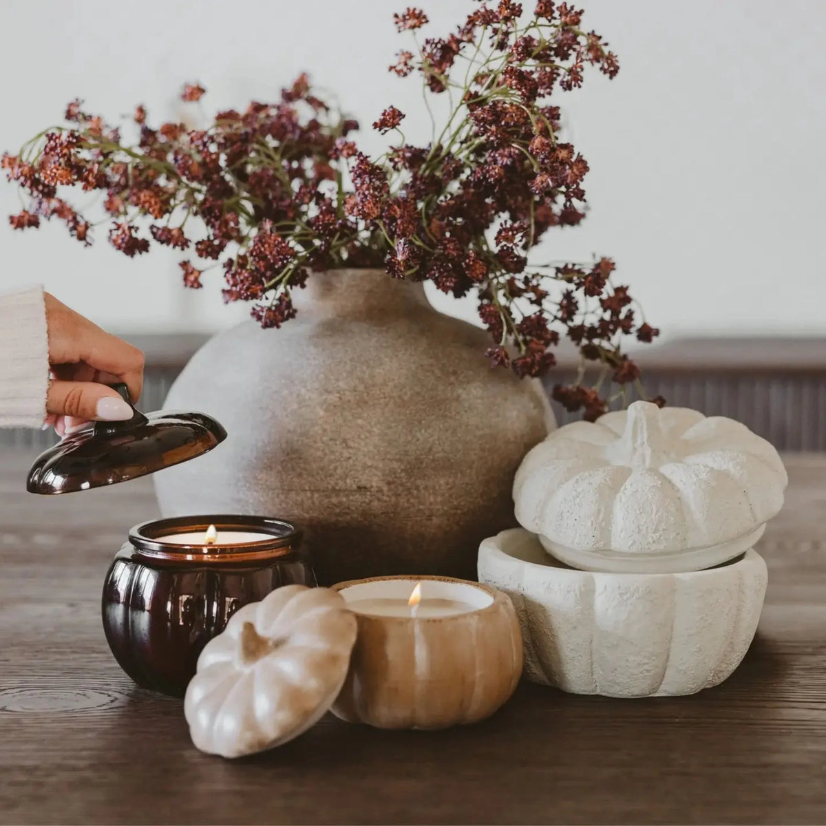 Decorative setting with a vase of flowers, candles, and pumpkin-shaped candles
