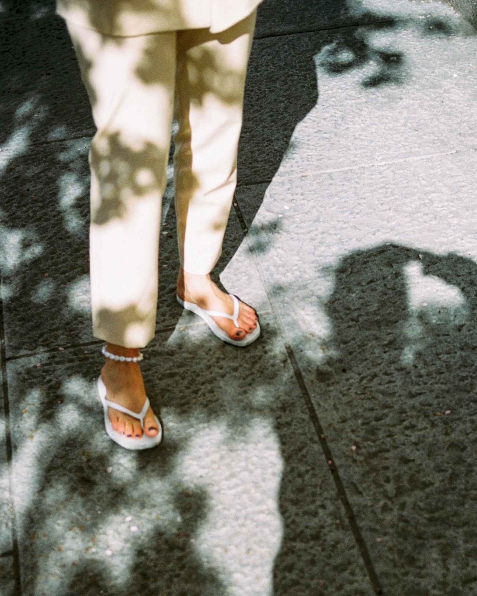 Person wearing white flip flop sandals and a pearl anklet