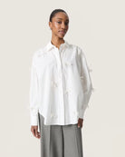 Woman wearing a white cotton blouse with bow details all over