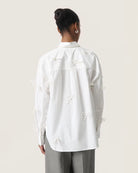 Woman wearing a white cotton blouse with bow details all over