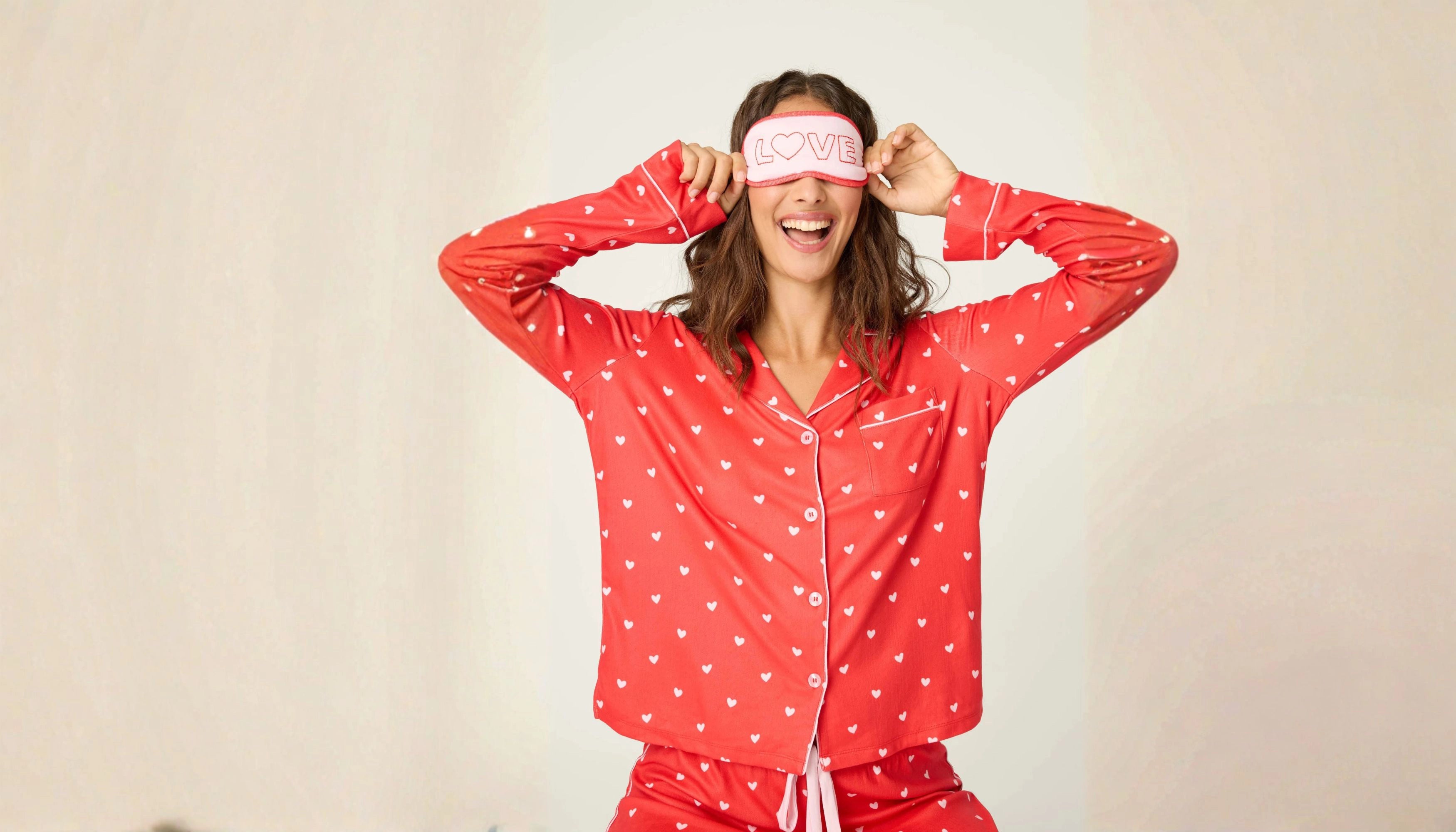 A woman wearing red polka dot heart pajamas and a matching eye mask that says 'Love' on it