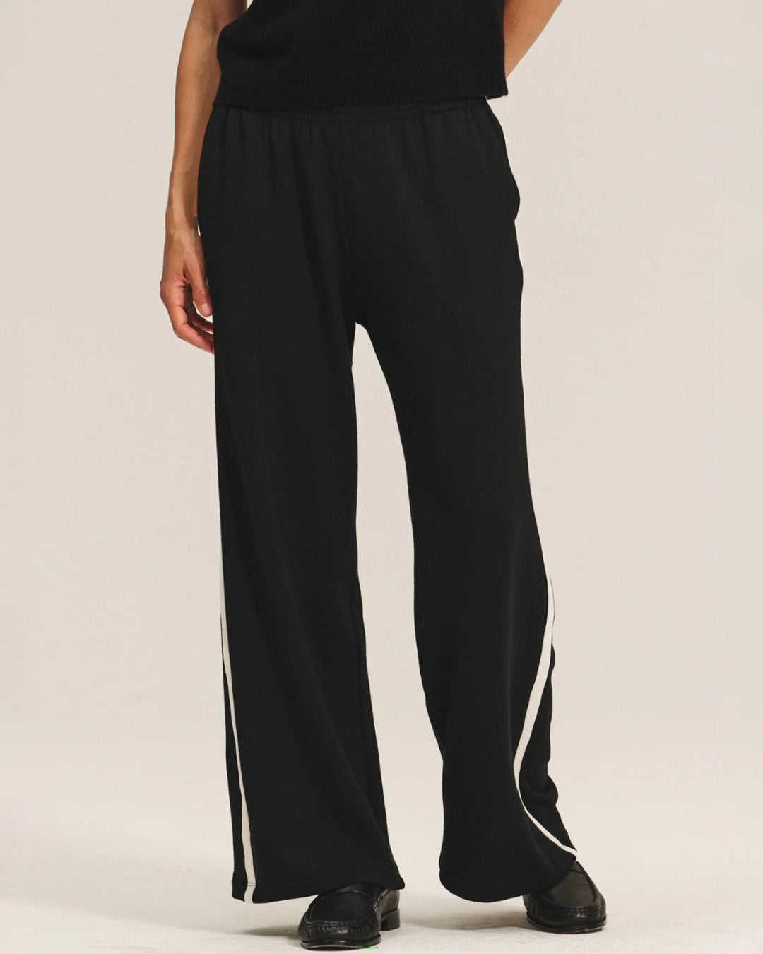 a woman wears a pair of fleece jogger pants in black with a cream stripe down the side