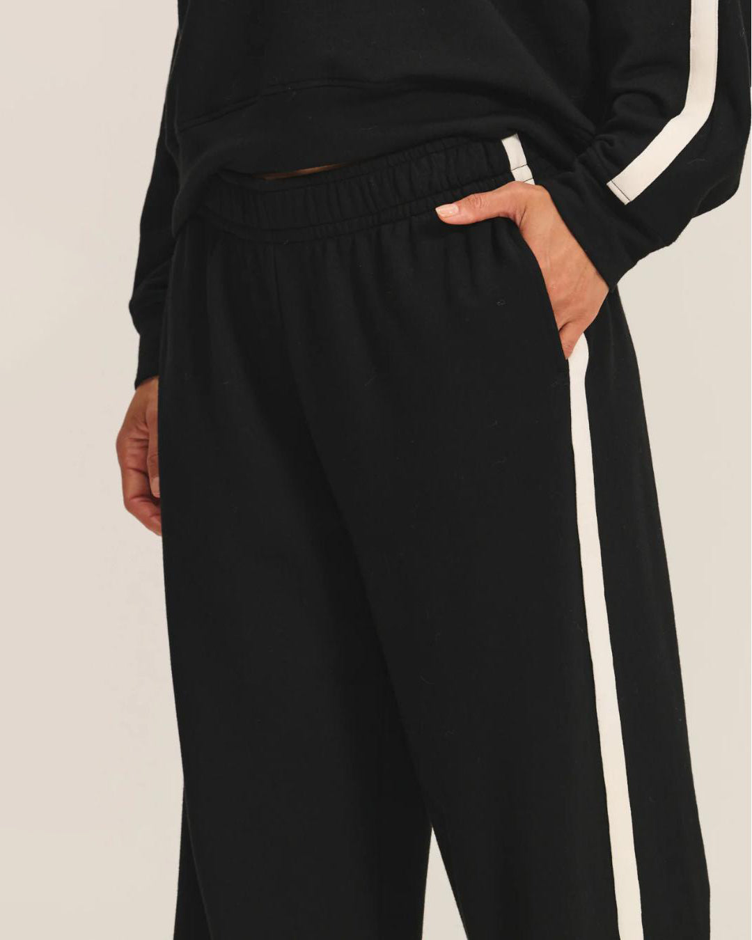 a woman wears a pair of fleece jogger pants in black with a cream stripe down the side