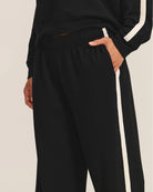 a woman wears a pair of fleece jogger pants in black with a cream stripe down the side