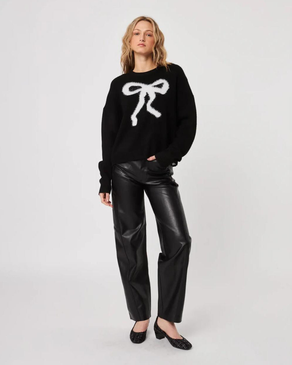 Woman wearing a black fluffy sweater with a white bow design and leather pants