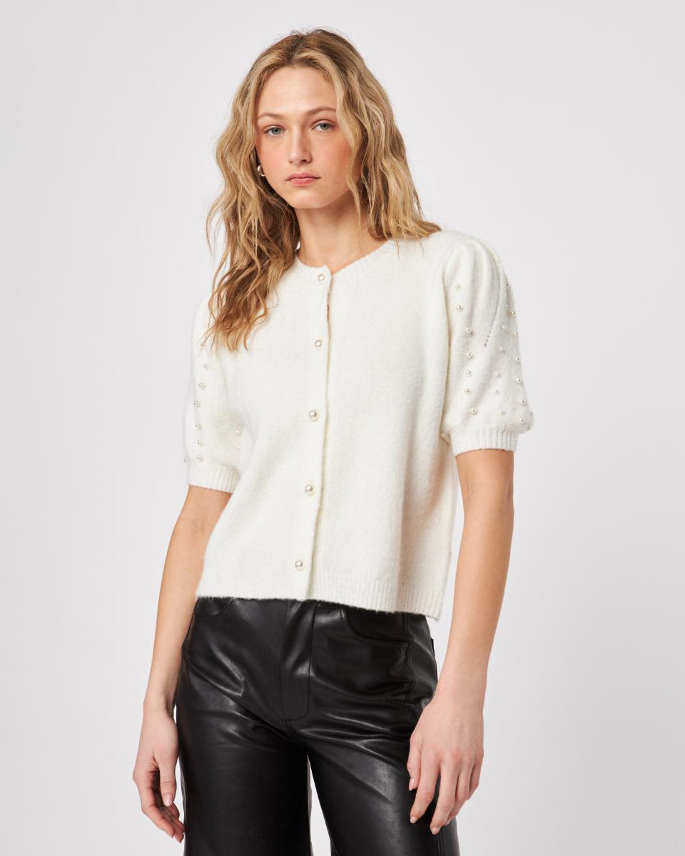 Woman wearing a white fluffy button down short sleeve cardigan with puff sleeves that have pearl embellishment on them