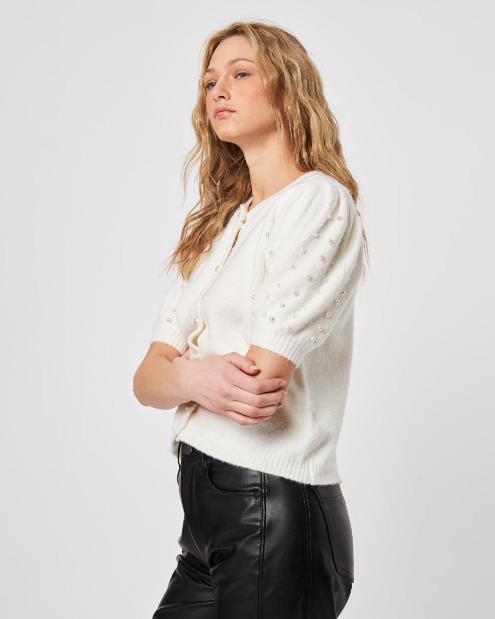 Woman wearing a white fluffy button down short sleeve cardigan with puff sleeves that have pearl embellishment on them