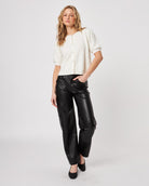 Woman wearing a white fluffy button down short sleeve cardigan with puff sleeves that have pearl embellishment on them and leather pants