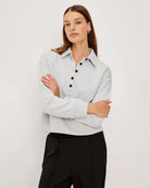 Woman wearing a light gray knit long-sleeve sweater with black buttons halfway down