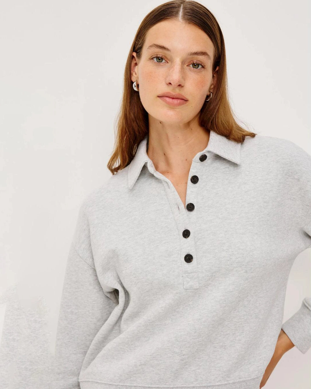 Woman wearing a light gray knit long-sleeve sweater with black buttons halfway down