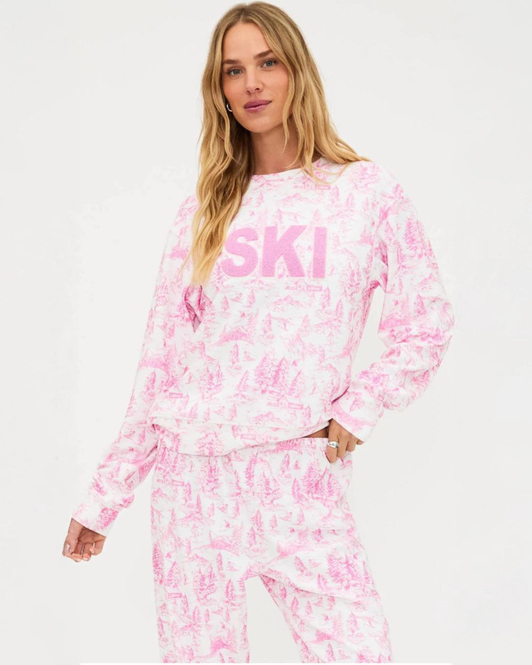 a woman wears a sweatshirt in white with pink toile ski pattern with the words 'SKI' on it