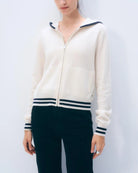 A woman wearing a white cashmere zip-up varsity style hoodie with navy accents