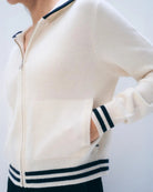 A woman wearing a white cashmere zip-up varsity style hoodie with navy accents