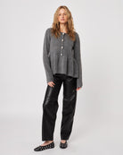 Woman wearing a gray peplum knitted  button down cardigan sweater with black leather pants