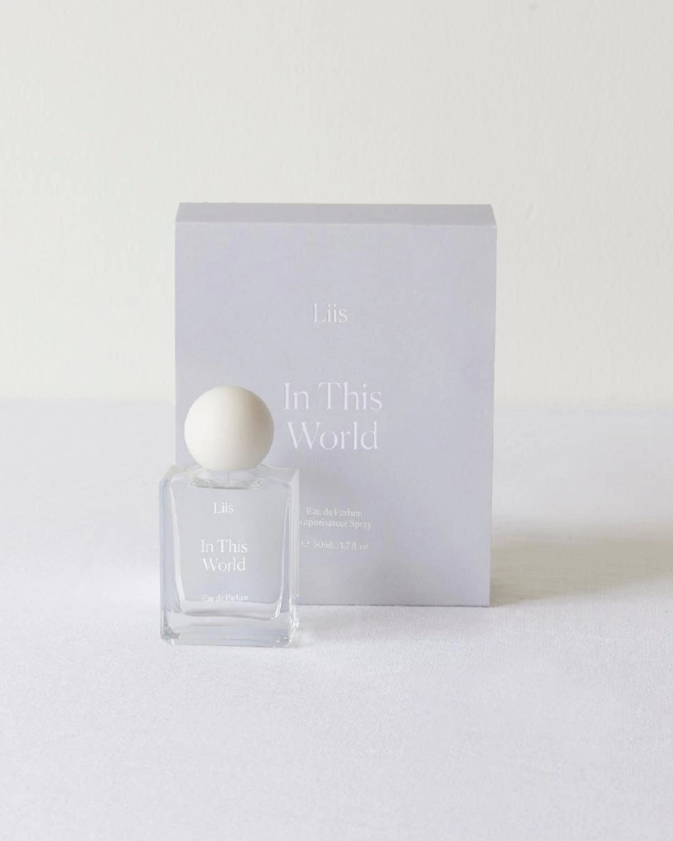Perfume bottle and packaging with 'In This World' branding on a white background