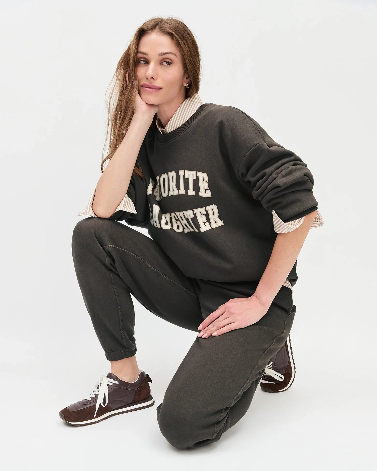 woman wearing dark brown sweatpants and sweater with 'favourite daughter' in varsity letters on them 