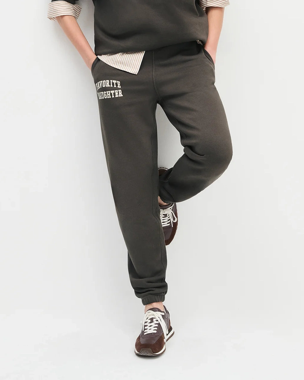 woman wearing dark brown sweatpants with 'favourite daughter' in varsity letters on them 