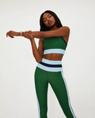 A woman wears a green racerback crop tank with light blue and navy on the bottom and sides