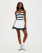 A woman wears a white pleated tennis skirt with navy and green stripe around the bottom