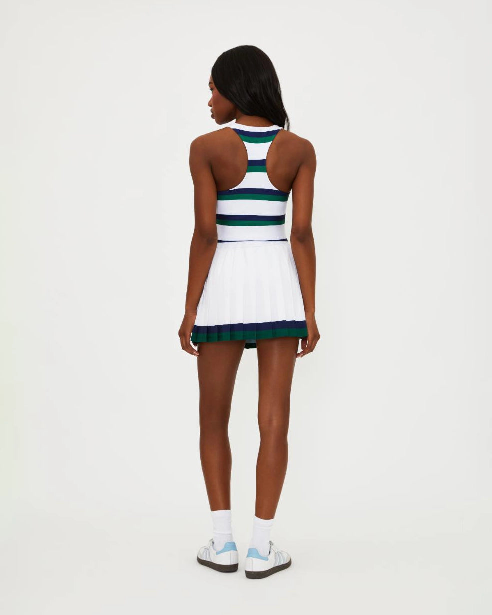 A woman wears a white pleated tennis skirt with navy and green stripe around the bottom