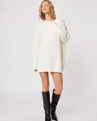 woman wearing a cable knit oversized sweater in cream with high leather boots