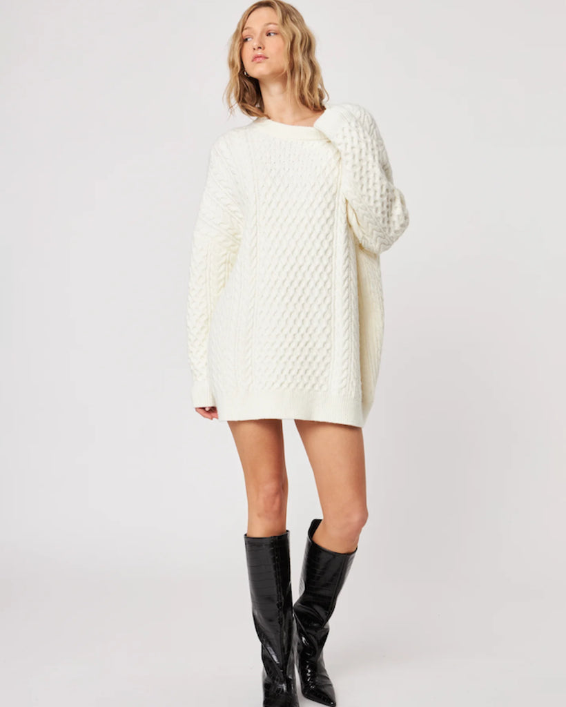 woman wearing a cable knit oversized sweater in cream with high leather boots