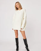 woman wearing a cable knit oversized sweater in cream with high leather boots