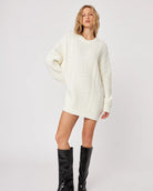 woman wearing a cable knit oversized sweater in cream with high leather boots