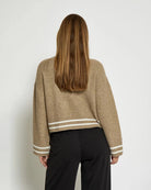 Woman wearing a beige knitted button down jacket with white trim