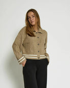 Woman wearing a beige knitted button down jacket with white trim