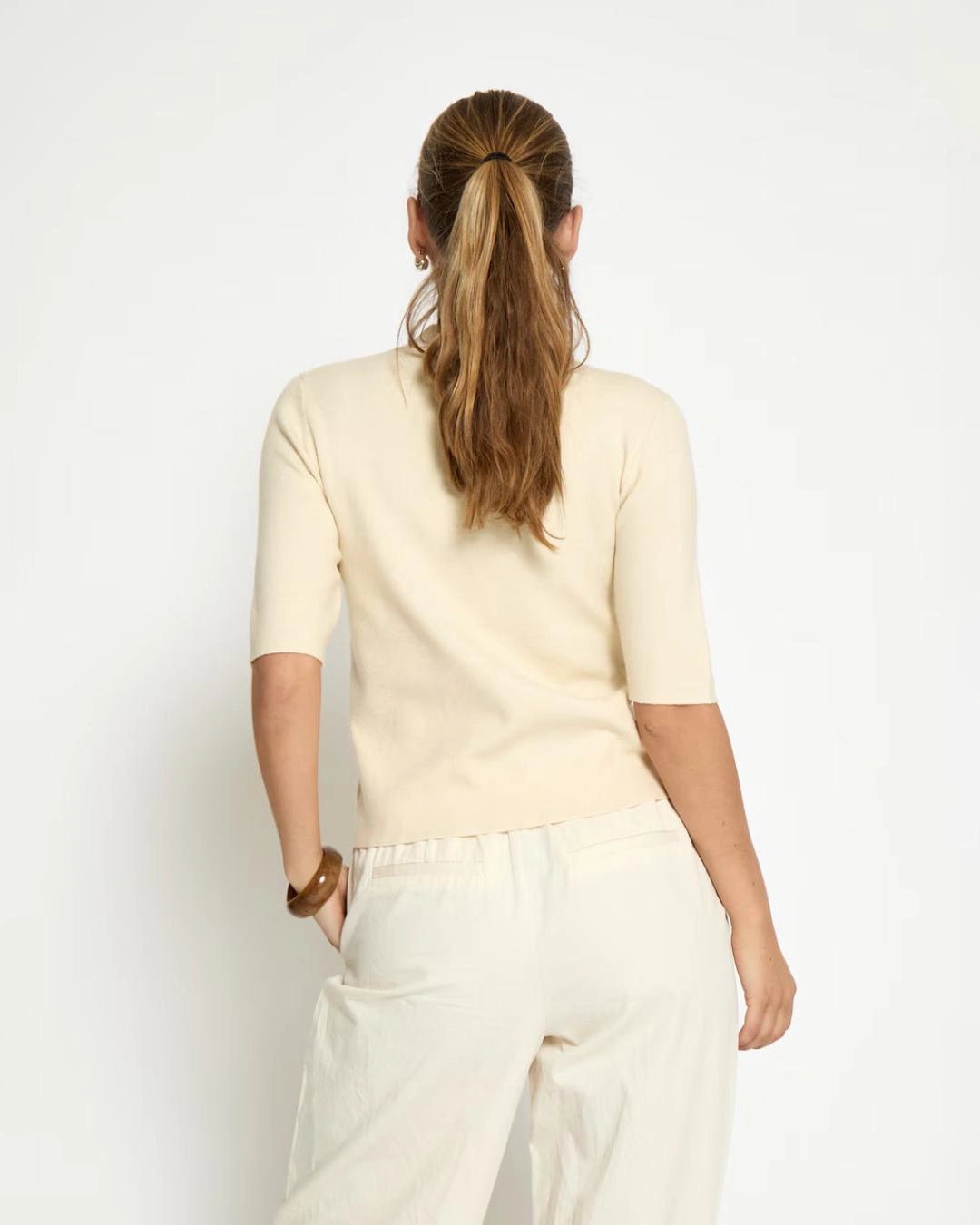 Woman wearing a cream short sleeve shirt with gold buttons 