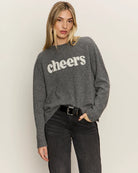 Woman wearing a gray cashmere sweater with 'cheers' text on it