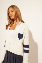 white knit cardigan with a navy heart on chest and two thick stripes on arms