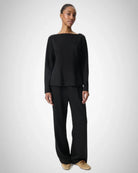 Woman wearing a black long-sleeve top with a boat neckline and matching trousers