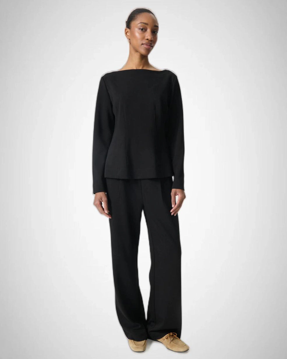 Woman wearing a black long-sleeve top with a boat neckline and matching trousers