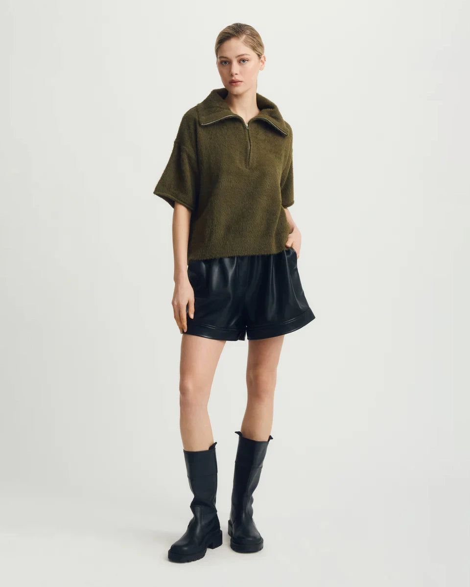 Woman wearing a green short-sleeve half zip sweater and black leather shorts with black boots